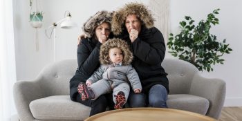 Couple Have Cold On The Sofa At Home With Winter Coat With Baby