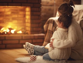 Family Mother And Child Hugs And Warm On Winter Evening By Fireplace